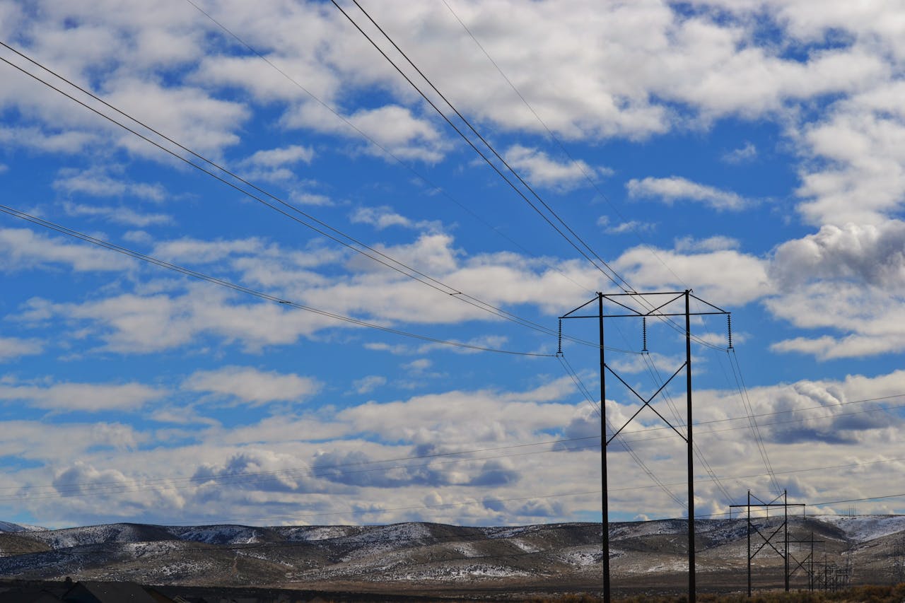 Power lines stretch across a vast landscape with blue skies and clouds, highlighting energy infrastructure.